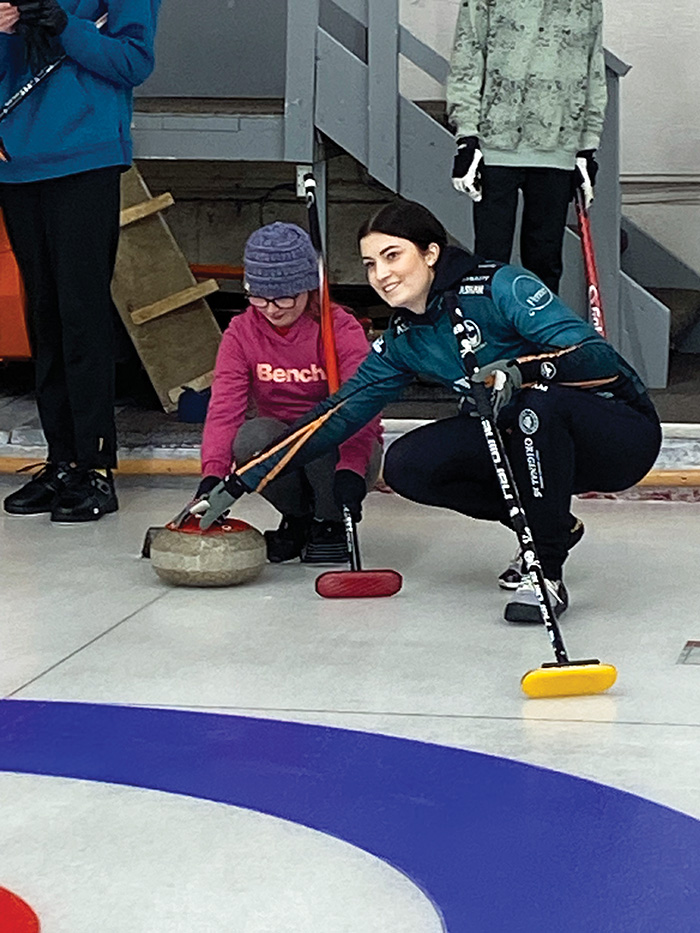 Rachel Erickson helping a curler prepare to deliver her rock.”></a><br />
<p class=
